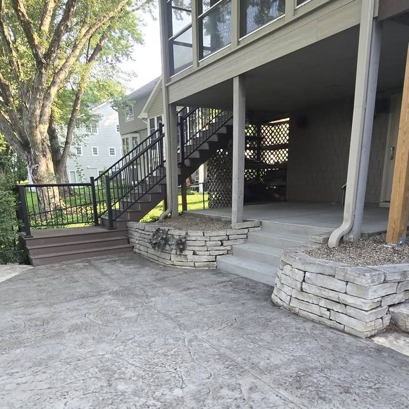 Stamped concrete patio under a raised deck with stone planter walls