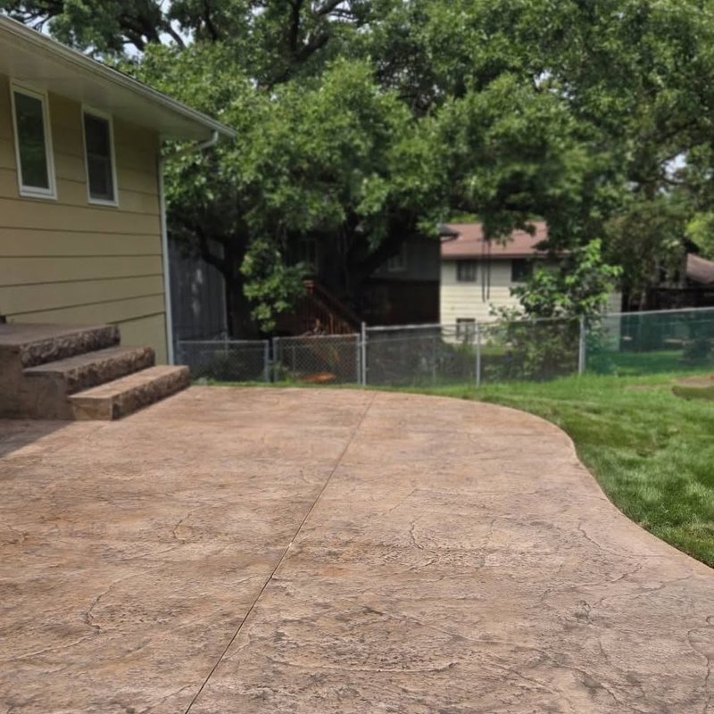 Curved stamped concrete backyard patio with stone steps beside a yellow house