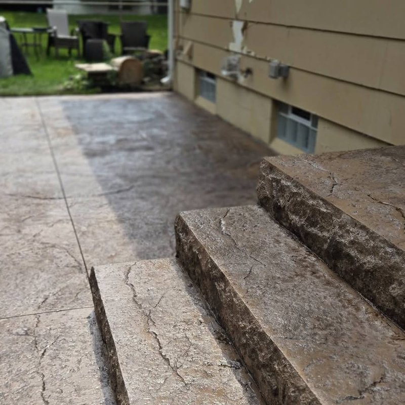 Close-up of rock-textured stamped concrete steps beside a patio