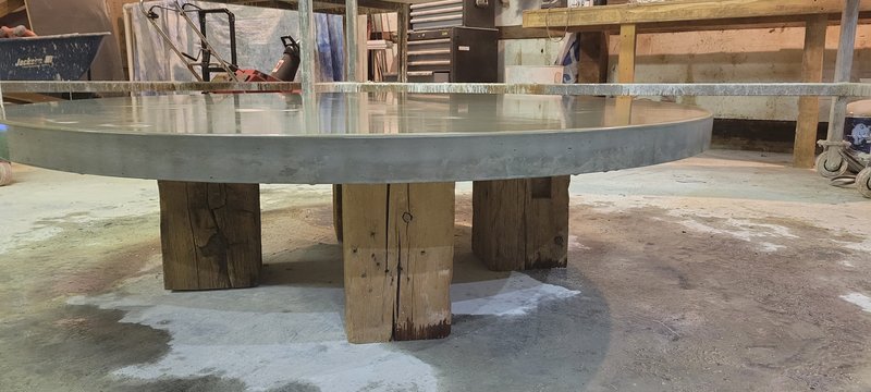 Round concrete table top with wood-grain edge on rustic timber legs