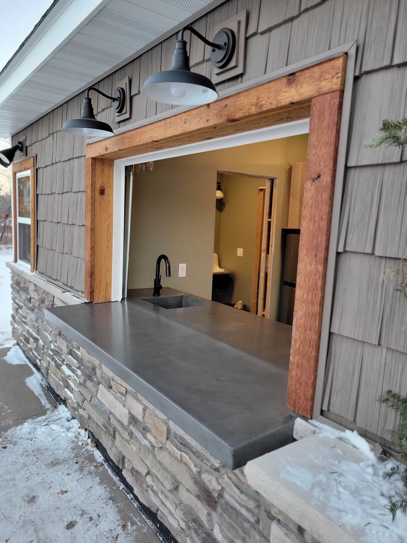 Exterior concrete pass-through bar counter framed by reclaimed wood and stone
