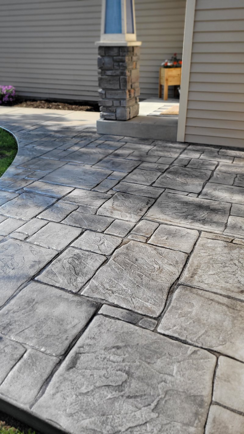 Stamped ashlar-pattern concrete patio leading to a stone-columned entry porch