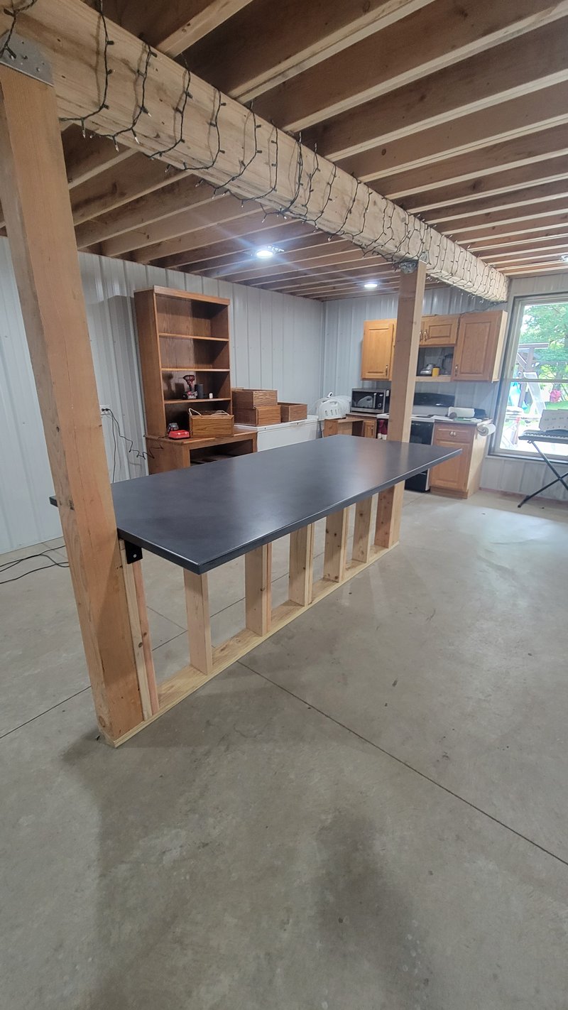 Dark concrete countertop on a wood-frame island in an unfinished kitchen