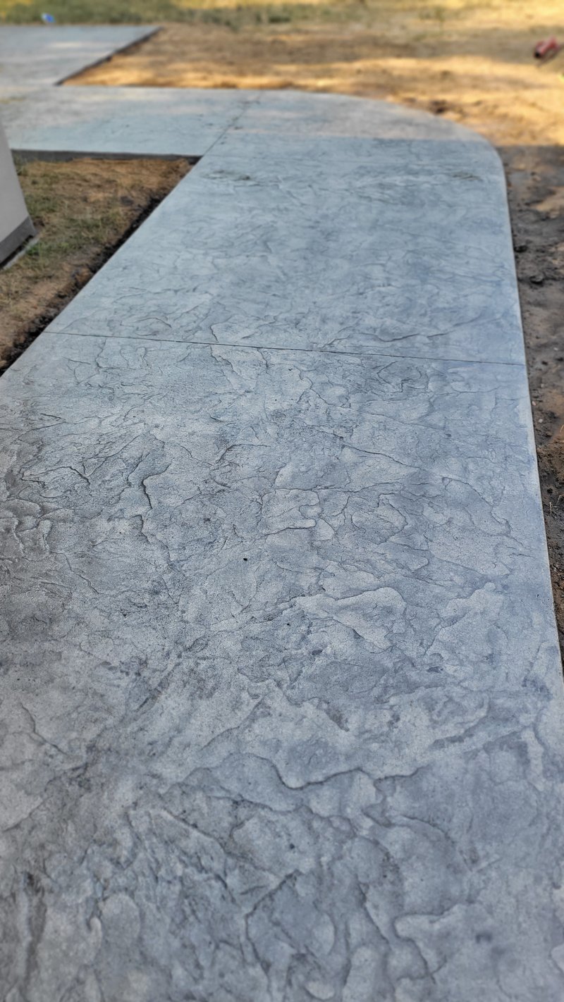 Stone-textured stamped gray concrete walkway curving through a yard