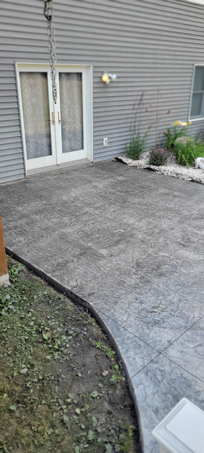 Charcoal stamped stone-pattern patio behind a gray-sided house