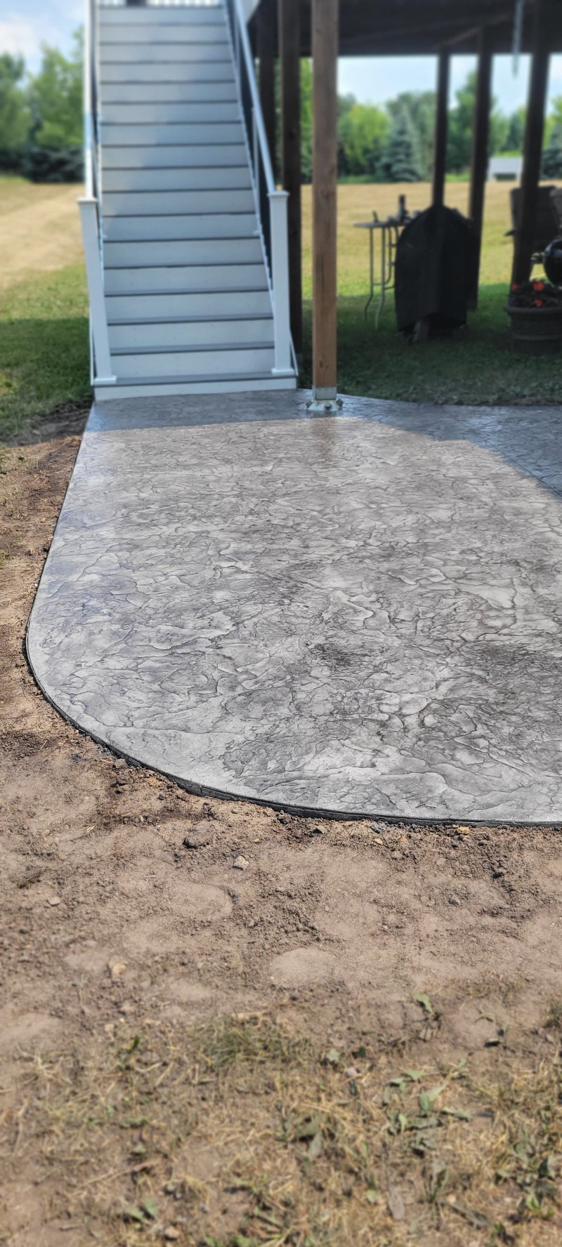 Oval stamped concrete patio beneath a deck with a white staircase