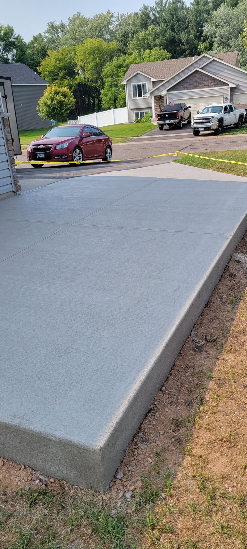 Broom-finished driveway slab with a red car and trucks in the background