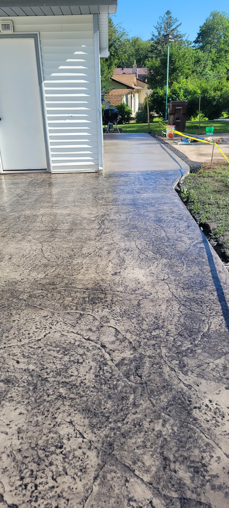Gray stamped concrete patio walkway curving beside a garage
