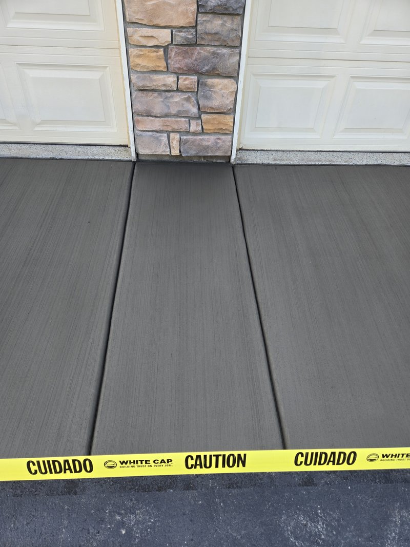Broom-finished driveway section between garage doors flanking a stone pillar