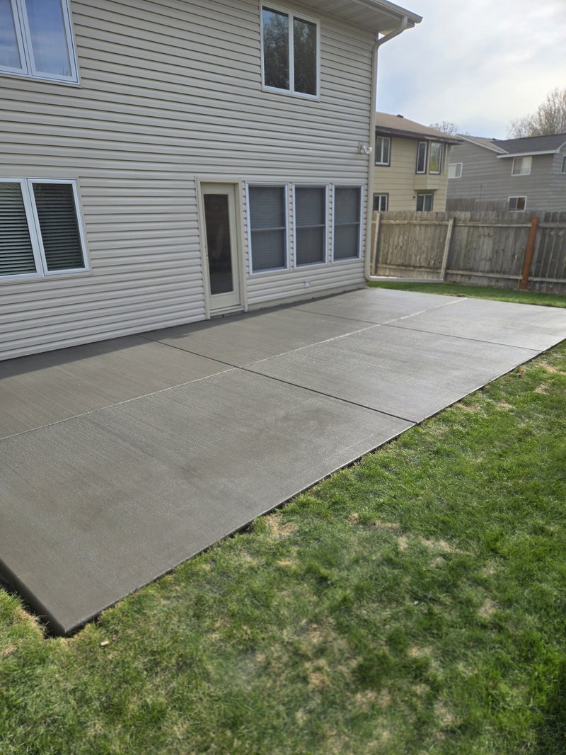 Broom-finished backyard patio slab beside a two-story tan vinyl-sided house