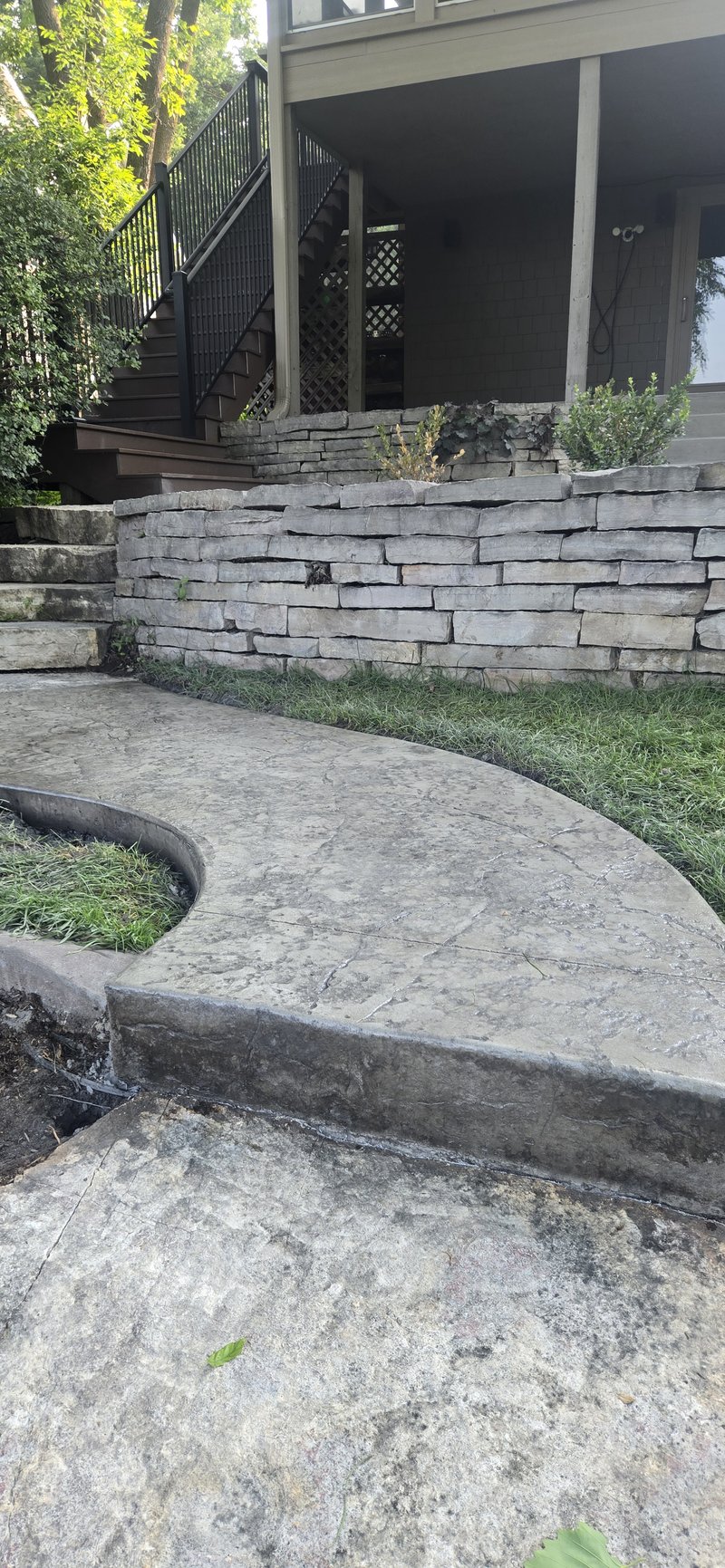 Curving stamped concrete walkway beside a stacked stone retaining wall