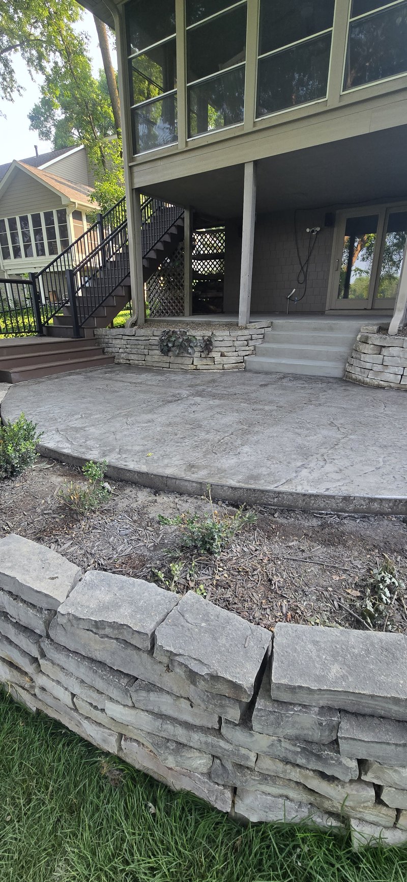 Round stamped concrete patio beneath an elevated deck with stone planter walls