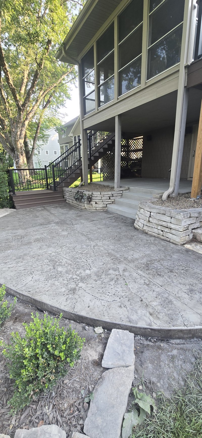 Round stamped concrete patio under a walkout deck with stone steps