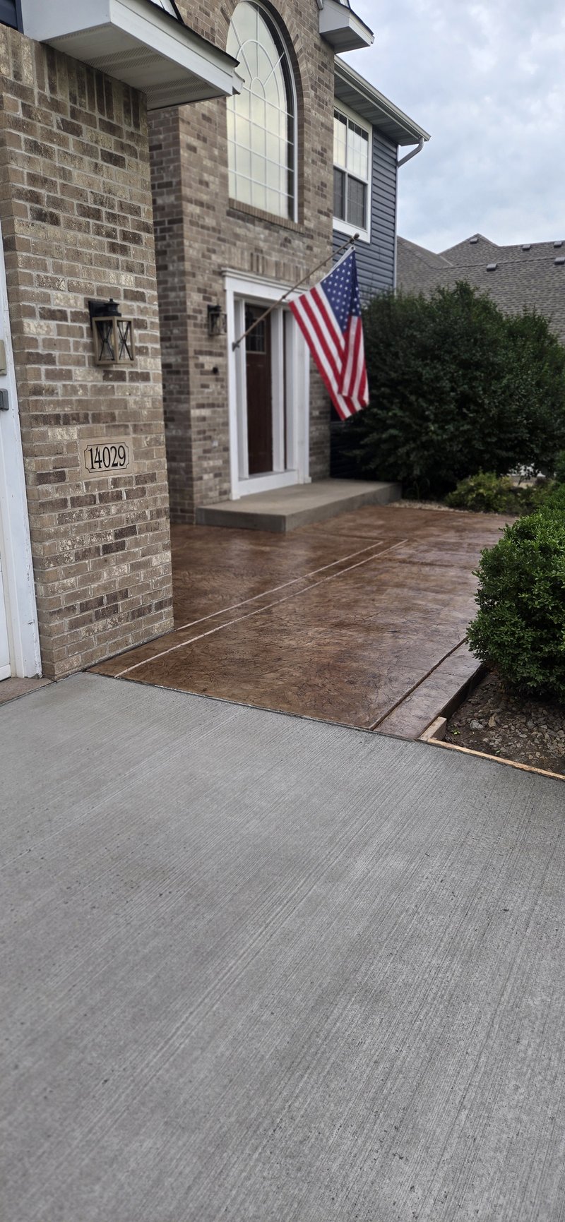 Brown stamped concrete entry walkway leading to a brick home