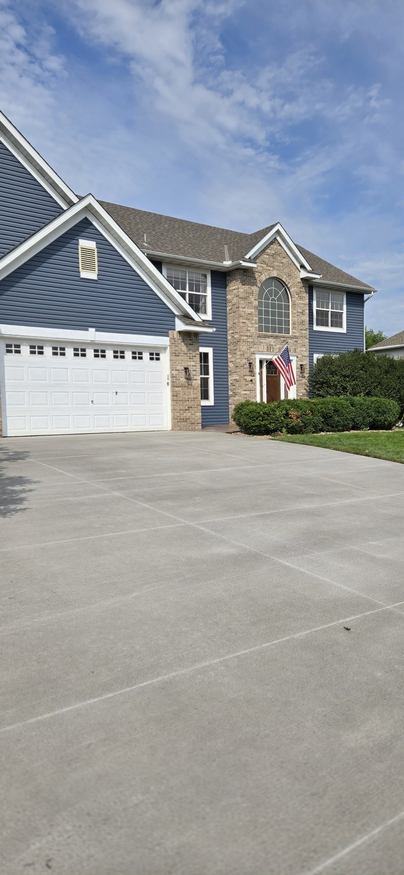 Broom-finished driveway in front of a two-story blue and brick home