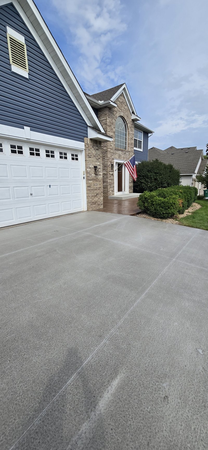 Broom-finished driveway alongside a blue and brick home with a stamped walkway