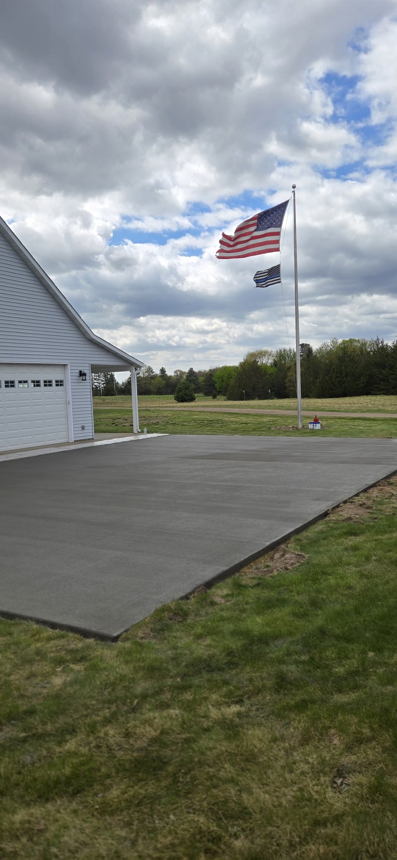 Broom-finished concrete driveway beside a white garage with an American flag