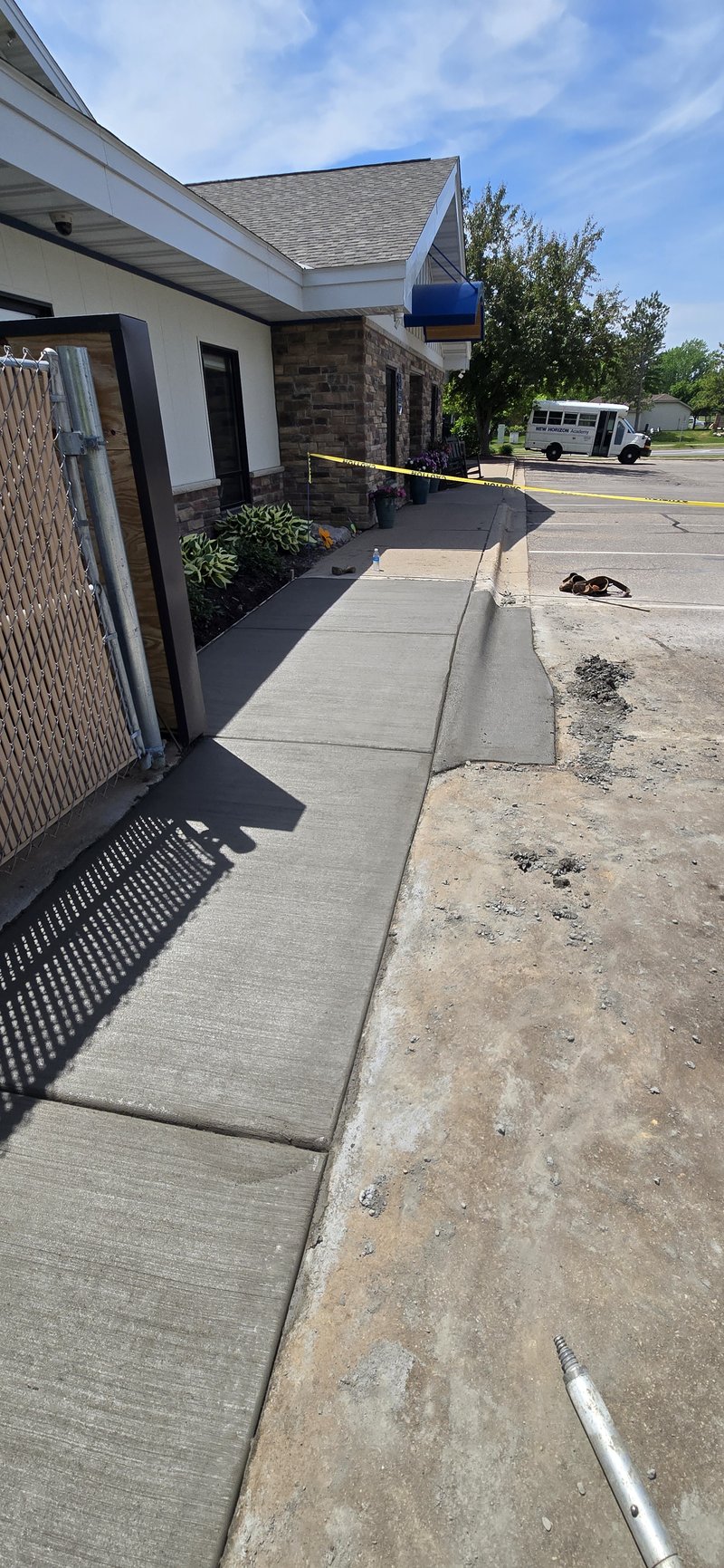 Broom-finished sidewalk along a stone-and-siding building next to a fresh curb cut
