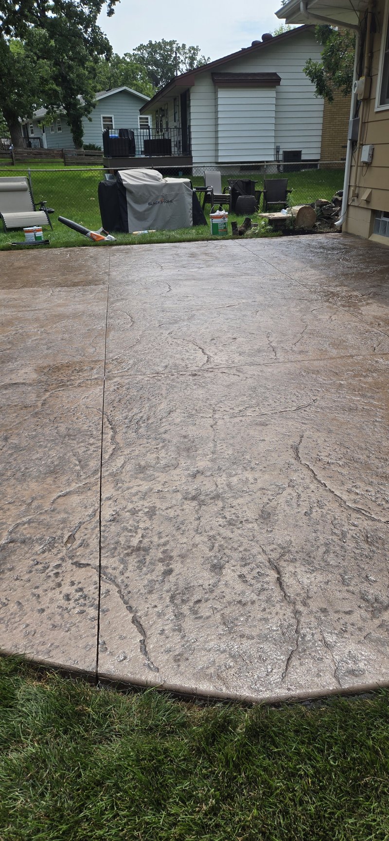 Wide stamped stone-pattern backyard patio slab with a grill and furniture