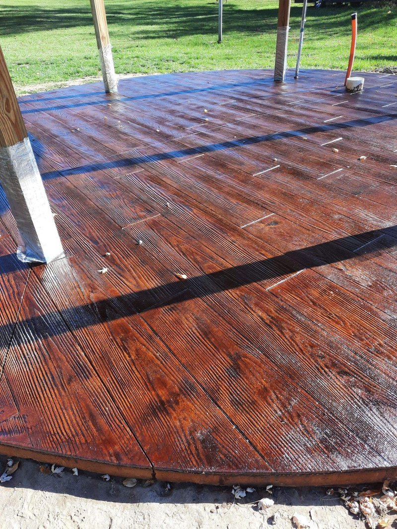 Circular stamped wood-plank pattern concrete patio stained reddish-brown
